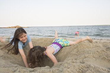 Schwestern spielen mit Sand am Strand gegen klaren Himmel - CAVF53418