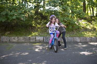 Mädchen, das seiner Schwester beim Fahrradfahren auf der Straße gegen Bäume im Park hilft - CAVF53420