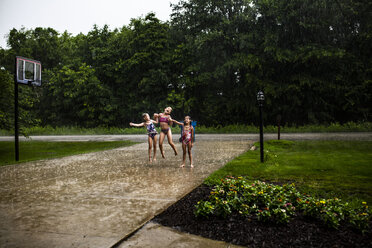 Verspielte Schwestern tanzen bei Regen in voller Länge auf dem Fußweg im Park - CAVF53422