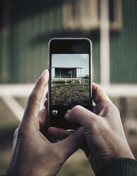 Abgeschnittene Hände eines Mannes, der ein Haus mit einem Mobiltelefon fotografiert - CAVF53445