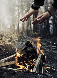 Ausgeschnittenes Bild eines Mannes, der sich im Winter die Hände am Lagerfeuer im Wald wärmt - CAVF53446