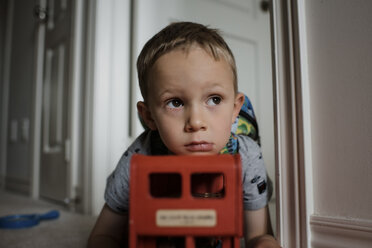 Nachdenklicher Junge schaut weg, während er sich zu Hause auf ein Spielzeug stützt - CAVF53478