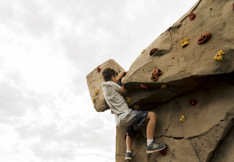Low angle view of boy climbing boulder against cloudy sky at playground - CAVF53500
