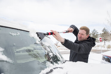 Mann reinigt im Winter Schnee von der Windschutzscheibe eines Autos - CAVF53505