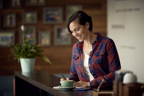 Smiling woman writing while standing in cafe stock photo