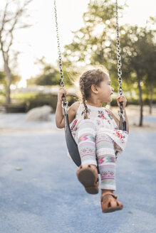 Glückliches Mädchen schaut beim Schaukeln auf dem Spielplatz weg - CAVF53543