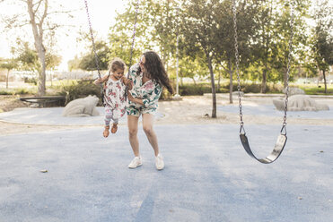 Happy mother pushing daughter swinging at playground - CAVF53544