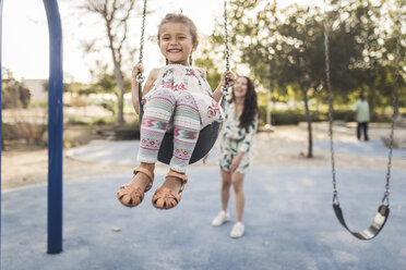 Happy mother pushing cute daughter swinging at playground - CAVF53546