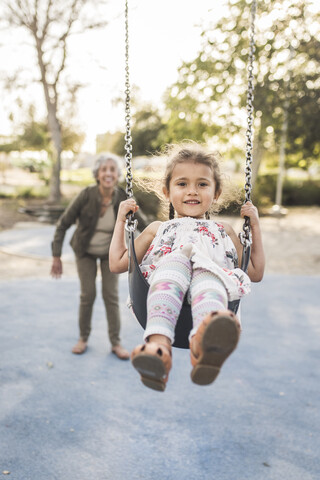 Glückliche Großmutter, die ihre Enkelin auf dem Spielplatz schaukeln lässt, lizenzfreies Stockfoto