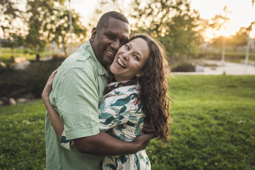 Portrait of cheerful couple embracing on field at park - CAVF53557