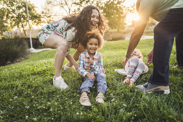 Parents playing with children on grassy field at park during sunset - CAVF53560