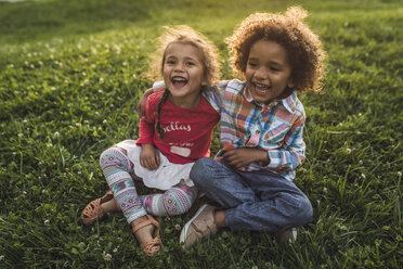 Cheerful siblings sitting on grassy field at park - CAVF53562