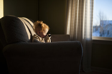 Baby-Junge spielt mit Spielzeug, während auf der Couch zu Hause bei Sonnenuntergang sitzen - CAVF53566