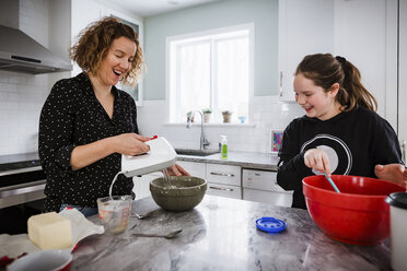Mutter mit Tochter mischen Teig in Schüsseln auf Kücheninsel zu Hause - CAVF53600