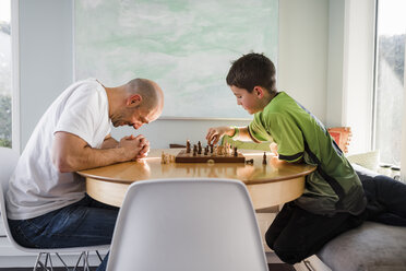 Father with son playing chess on table at home - CAVF53603