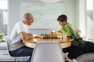 Side view of father with son playing chess on table at home - CAVF53604