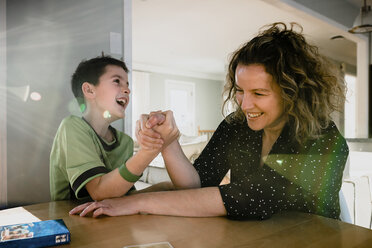 Spielerische Mutter Armdrücken mit Sohn auf Tisch zu Hause - CAVF53613