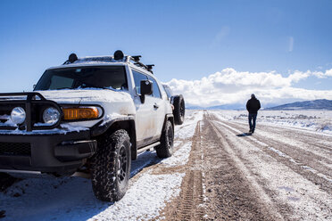 Rear view of man with off-road vehicle on dirt road amidst desert during winter - CAVF53620