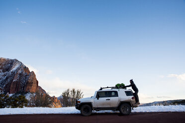 Side view of man putting backpack on off-road vehicle at desert against sky during winter - CAVF53627