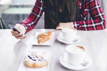 Mittelteil einer Frau mit Frühstück auf dem Tisch, die ein Mobiltelefon in einem Café benutzt - CAVF53636