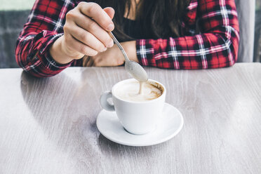 Mittelteil einer Frau, die Kaffee mit einem Löffel auf einem Tisch in einem Café mischt - CAVF53637