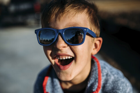 Nahaufnahme eines glücklichen Jungen mit Sonnenbrille, der im Freien sitzt - CAVF53664