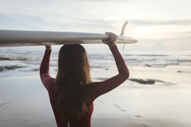 Rückansicht einer jungen Frau, die ein Surfbrett auf dem Kopf trägt, während sie am Strand steht - CAVF53669