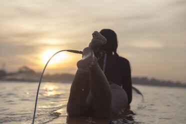 Junge Frau in voller Länge auf einem Surfbrett im Meer liegend gegen den Himmel bei Sonnenuntergang - CAVF53670