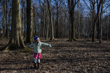 Happy girl with arms outstretched standing on field in forest - CAVF53692