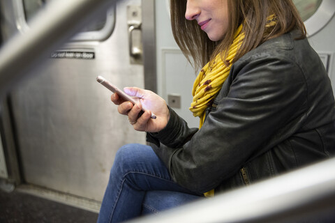 Mittelteil einer Frau, die während einer Zugfahrt ein Mobiltelefon benutzt, lizenzfreies Stockfoto