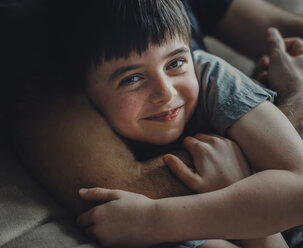 Midsection of father embracing happy son while lying on sofa at home - CAVF53767