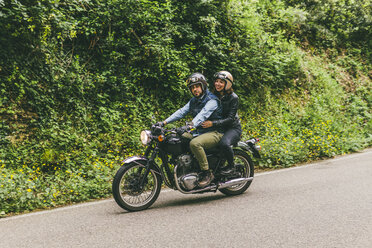 Motorrad fahrendes Paar auf der Straße inmitten von Bäumen im Wald - CAVF53771