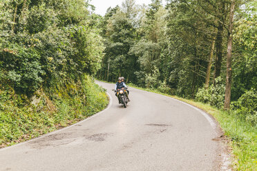 Couple riding on motorcycle in forest - CAVF53773