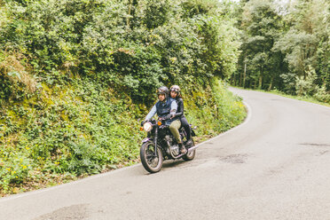 Paar fährt Motorrad auf der Straße zwischen Bäumen und Pflanzen im Wald - CAVF53774