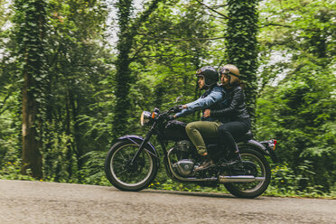 Seitenansicht eines Motorrad fahrenden Paares auf einer Straße mit Bäumen und Pflanzen im Wald - CAVF53775