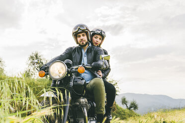 Porträt eines Paares auf einem Motorrad sitzend gegen den Himmel - CAVF53778