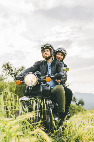 Paar schaut weg, während es auf einem Motorrad gegen den Himmel sitzt, lizenzfreies Stockfoto