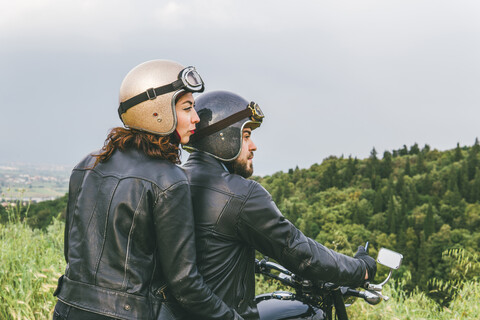 Rückansicht eines Paares, das auf einem Motorrad sitzt und in den Himmel schaut, lizenzfreies Stockfoto