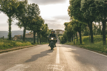 Couple riding motorcycle on road amidst trees against sky during sunset - CAVF53784