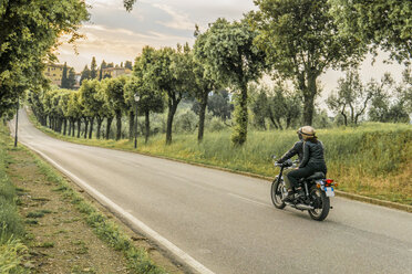 Couple riding motorcycle on road amidst trees during sunset - CAVF53785