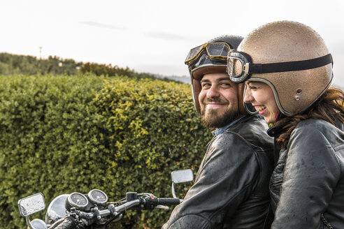 Glückliches Paar im Gespräch auf dem Motorrad sitzend gegen den Himmel - CAVF53788