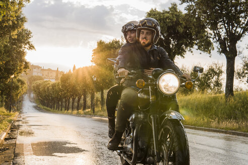 Paar, das auf dem Motorrad sitzend gegen den Himmel bei Sonnenuntergang wegschaut - CAVF53793