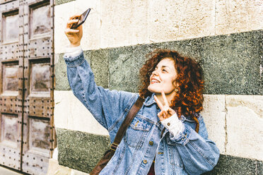 Frau, die ein Selfie mit ihrem Smartphone macht, während sie an der Wand steht - CAVF53799