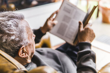 Hoher Blickwinkel eines Mannes, der ein Buch liest, während er zu Hause auf einem Sessel sitzt - CAVF53811