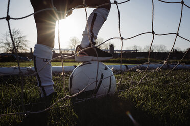 Tiefschnitt eines Mannes mit Fußball, der auf einer Wiese am Netz steht - CAVF53855