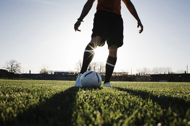 Niedriger Ausschnitt eines Fußball spielenden Mannes auf einer Wiese gegen den klaren Himmel bei Sonnenuntergang - CAVF53856