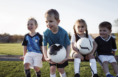 Children looking away while sitting on bench against clear sky at park during sunset - CAVF53857