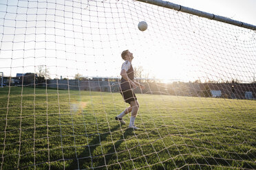 Man practicing soccer at park seen through net during sunset - CAVF53860
