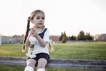 Girl with trophy looking away while sitting on bench against clear sky at park - CAVF53862