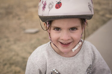 Hochformatiges Porträt eines glücklichen Mädchens, das einen Fahrradhelm trägt und auf der Straße steht - CAVF53895